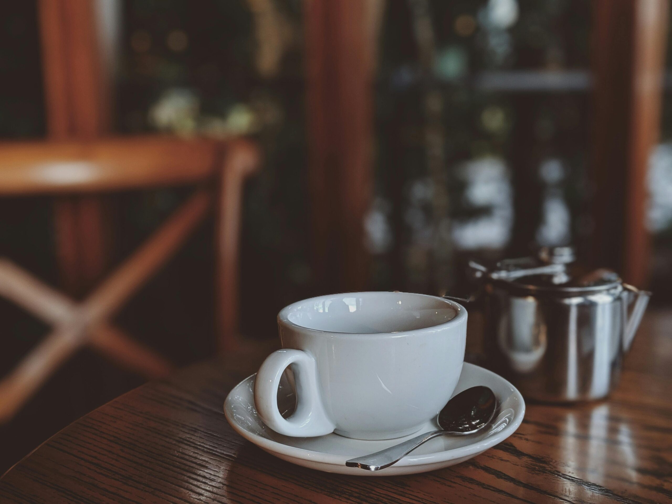 Warm café atmosphere featuring a coffee cup and metal teapot on a wooden table.