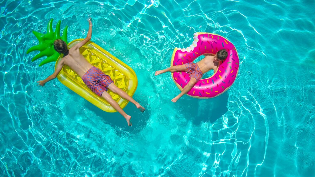 Two children lay on colorful floaties in a vibrant turquoise swimming pool, enjoying a summer day.